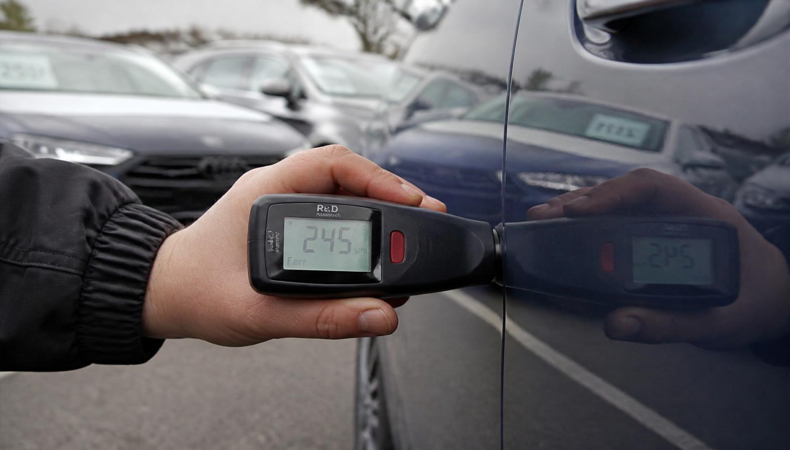 Close-up of a paint-depth gauge reading 245 microns on a used car door panel at a Lansvale dealer yard